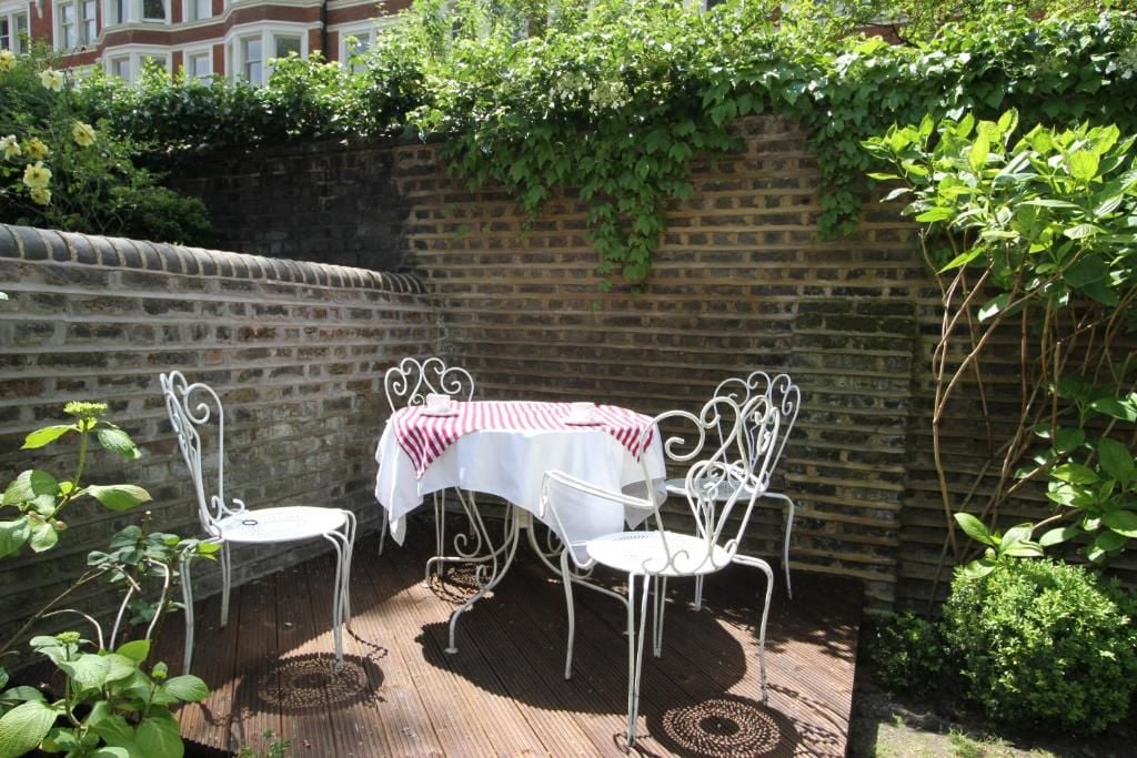 Un patio con mesa y sillas, un muro de ladrillo y follaje.