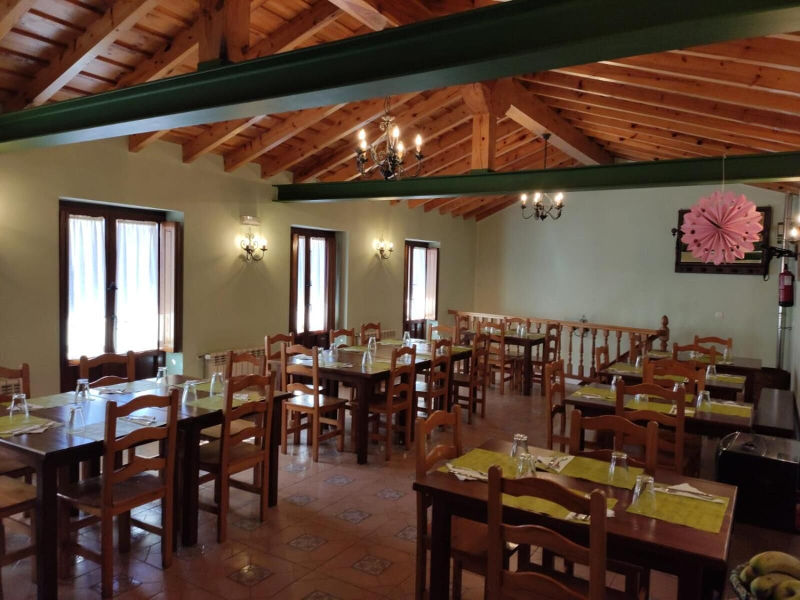 A dining area with wooden tables and chairs, a high wooden ceiling, and wall-mounted lights.