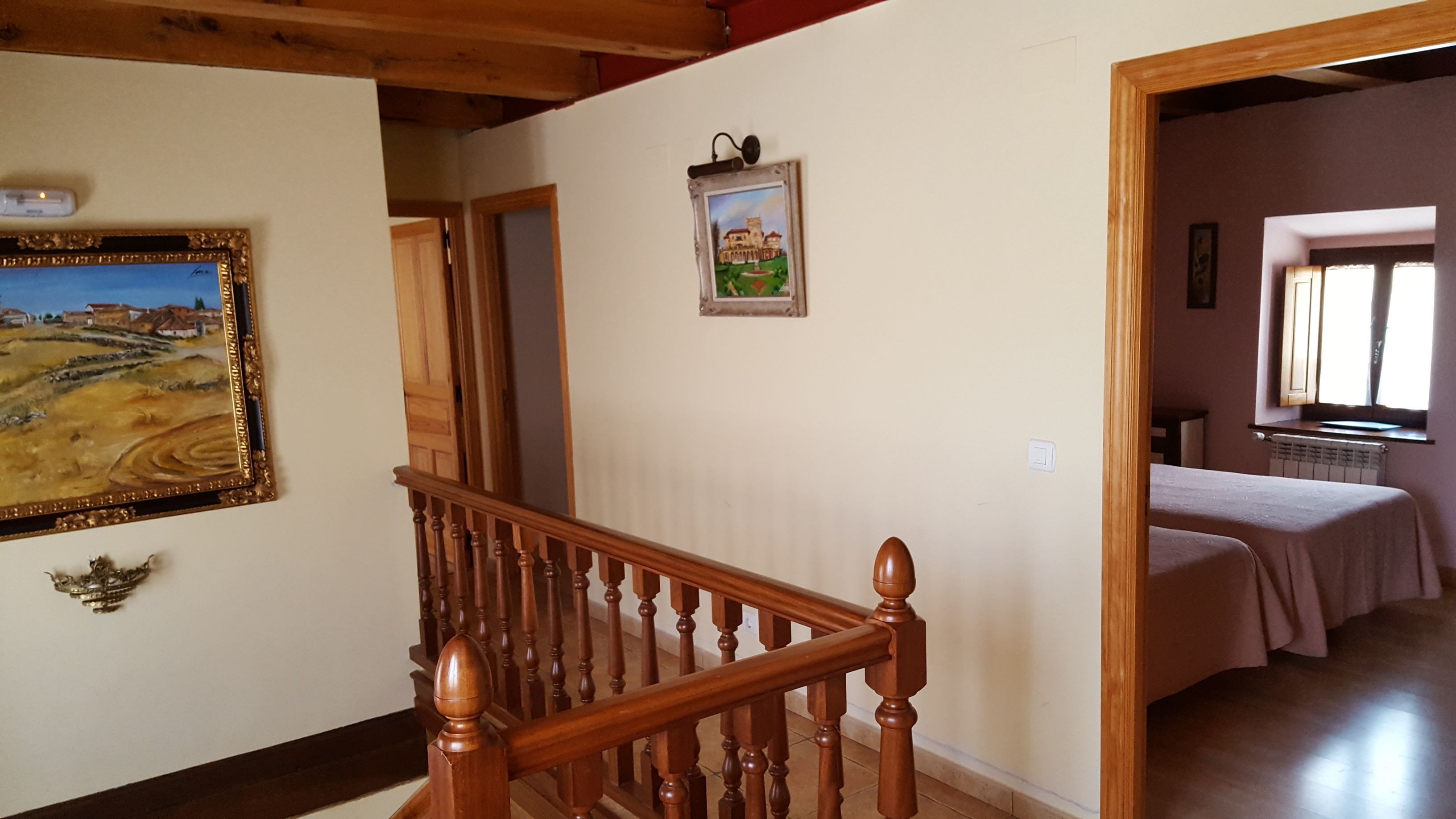 Una escalera con barandilla de madera que lleva a un dormitorio con cama y ventana.