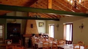 A dining area with wooden tables and chairs, a stone fireplace, and a chandelier.