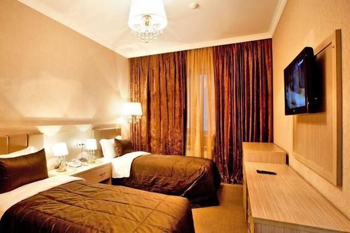 A hotel room with two beds, a desk, a television, and a chandelier.
