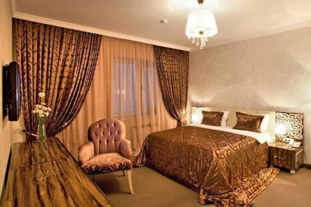 A hotel room with a large bed, a chair, a bedside table, and a floor lamp.