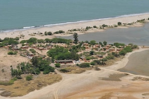 Luftaufnahme eines Küstendorfes mit traditionellen Hütten, einem Sandstrand und einer unbefestigten Straße.