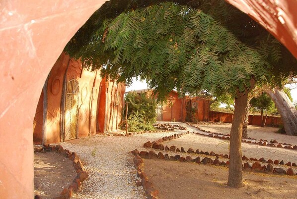 An arched corridor with a gravel path, surrounded by red walls and trees. - Ecolodge de Palmarin (Fatick)