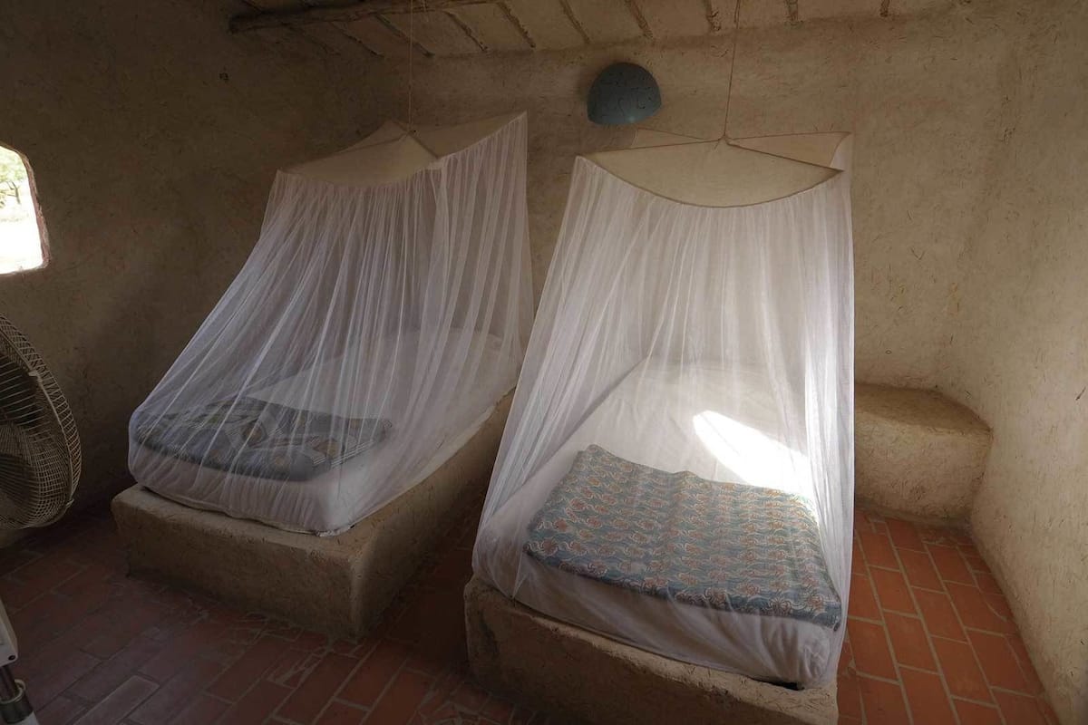 Two single beds with mosquito netting, a fan, and a brick floor.