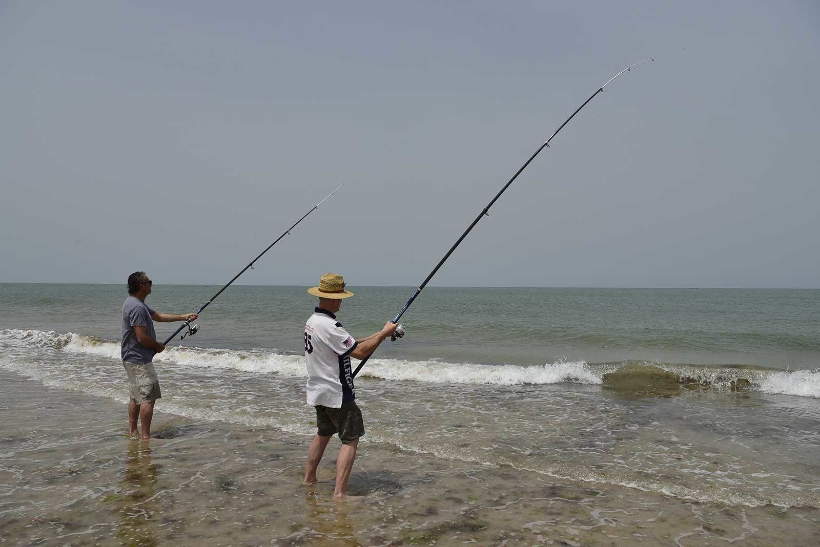 Två personer fiskar på stranden, med sina fiskespön i vattnet.
