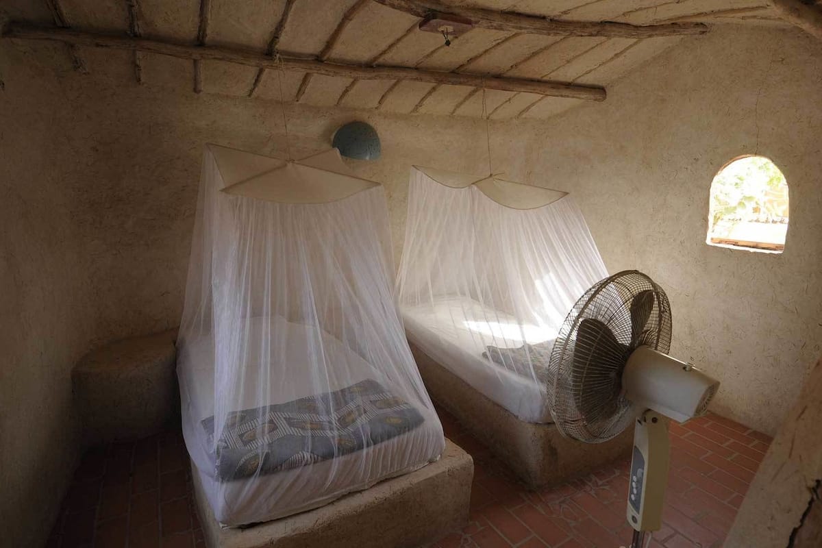A room with two beds covered by mosquito netting, a standing fan, and a small window.