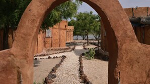 A pathway leading through a rustic archway, surrounded by trees and a building with a traditional design. - Ecolodge de Palmarin (Fatick)