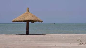 Una playa con un paraguas de paja y un bote en el agua.