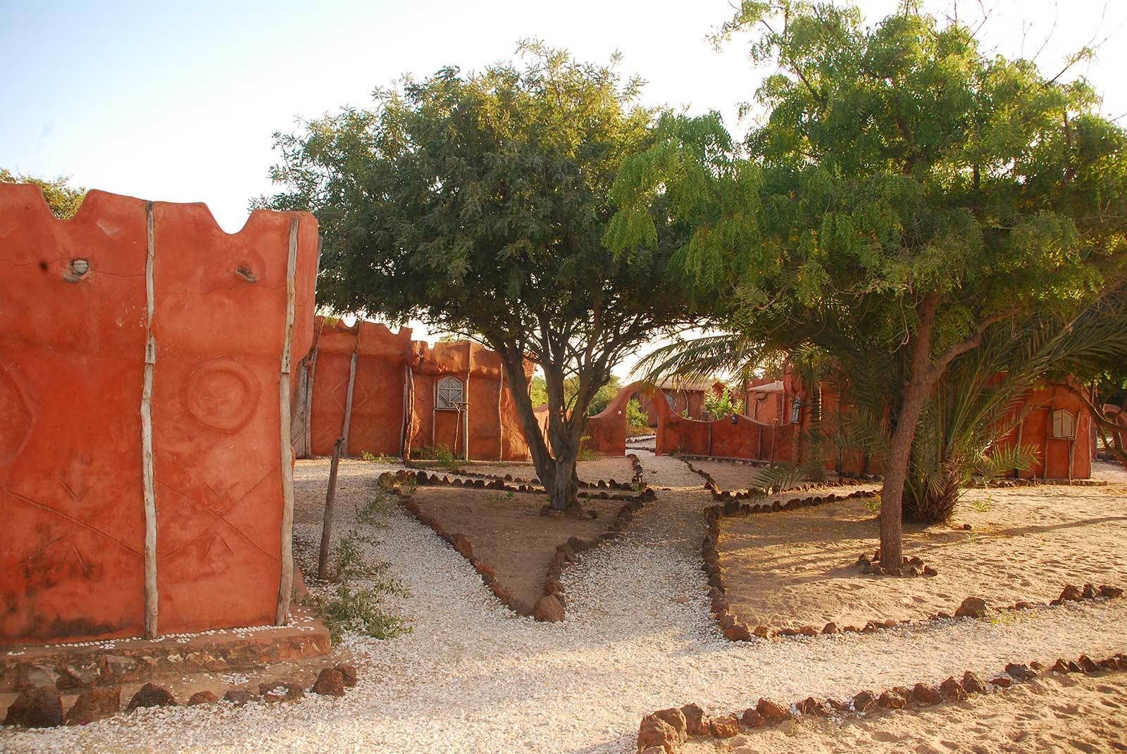 A desert landscape with traditional red-roofed structures, gravel paths, and sparse vegetation.