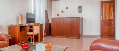 Amplia sala de estar con una mesa de centro de vidrio, sofá de cuero, escritorio de madera y televisión.