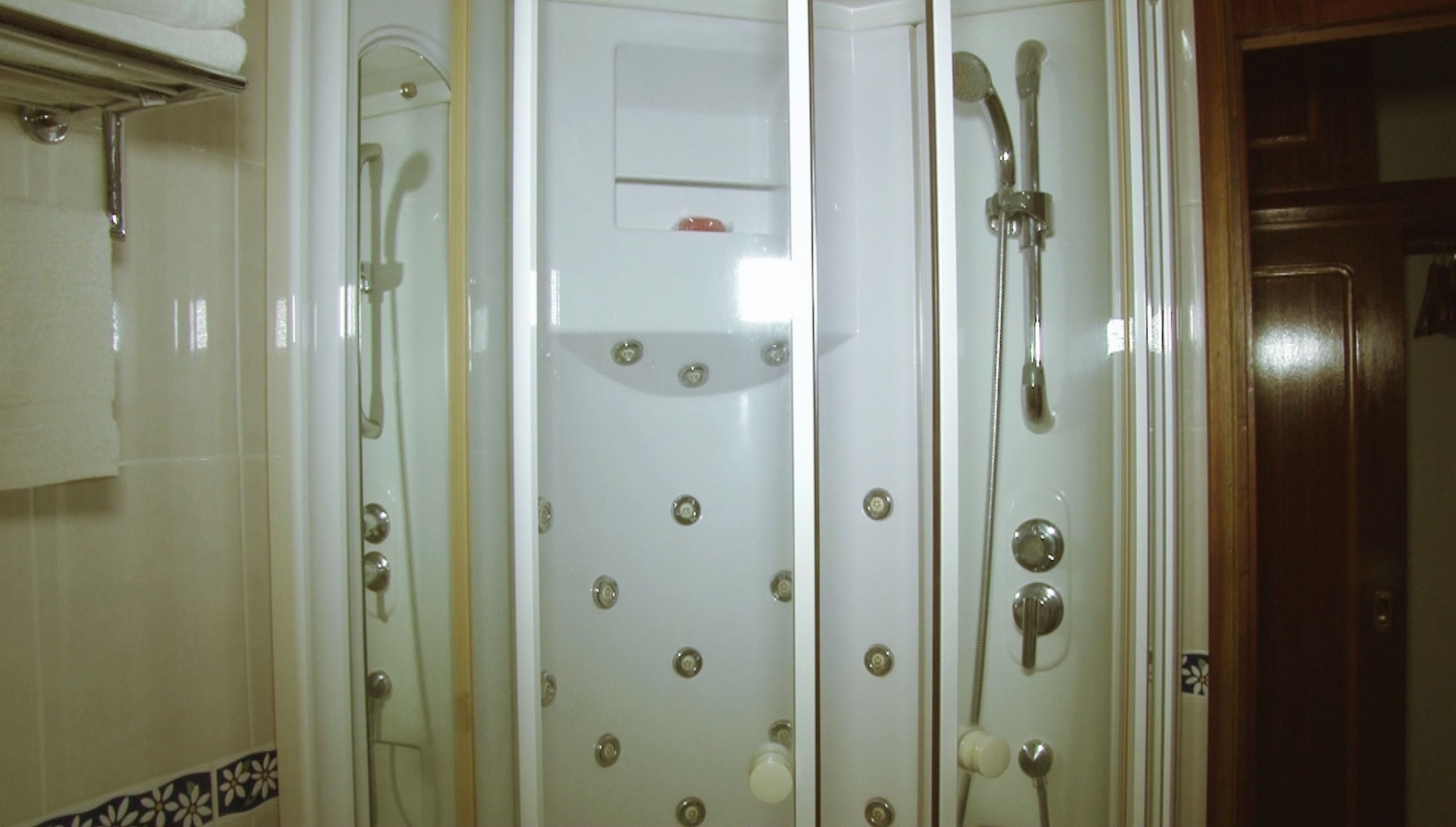 Un bagno con box doccia in vetro, parete rivestita in piastrelle bianche e porta in legno.
