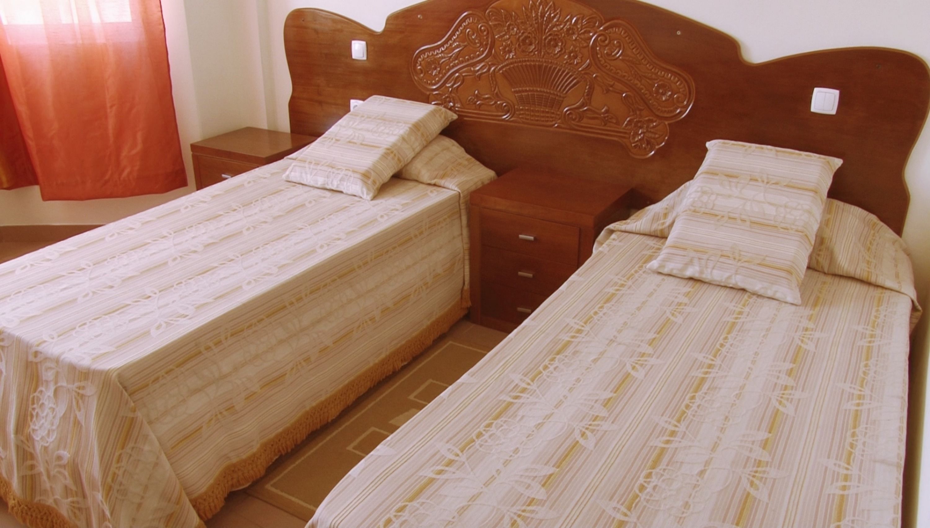 Twin beds with wooden headboards, a nightstand, and a red curtain.