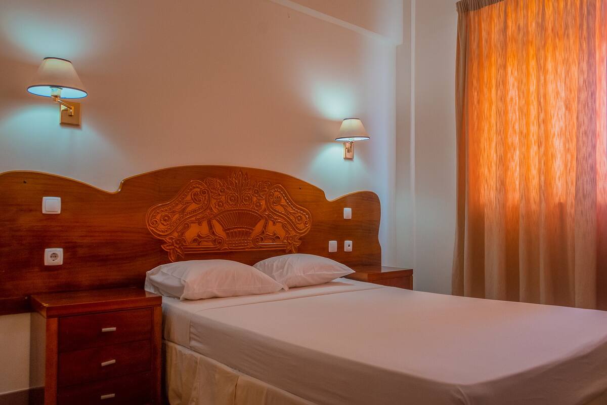 A neatly made bed with a wooden headboard, two bedside tables, and wall-mounted lamps.