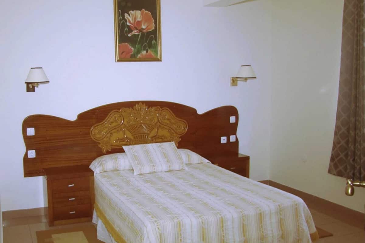 A bedroom with a wooden headboard, a single bed with a striped bedspread, two bedside lamps, and a painting on the wall.