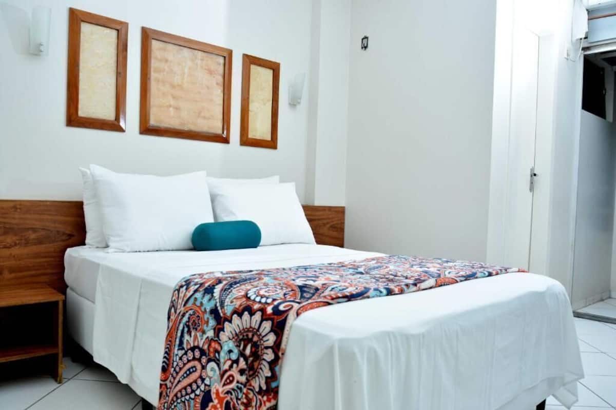 Una cama con ropa blanca, una manta de colores y un cabecero de madera.