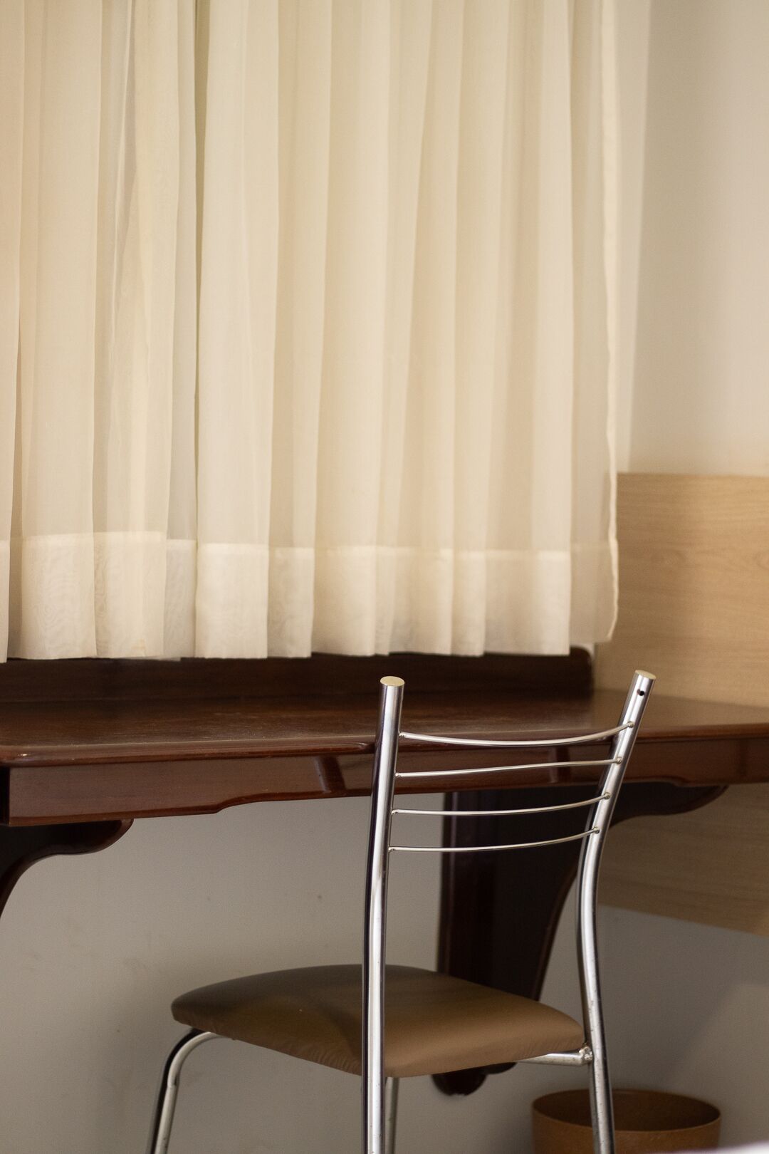 A chair with a metal frame and a cushioned seat, positioned in front of a window with a white curtain.