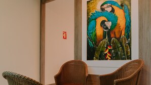 Un hall con sillas de mimbre, un cuadro enmarcado de loros y un extintor en la pared.