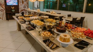 Una mesa de buffet con distintos alimentos y un televisor al fondo.