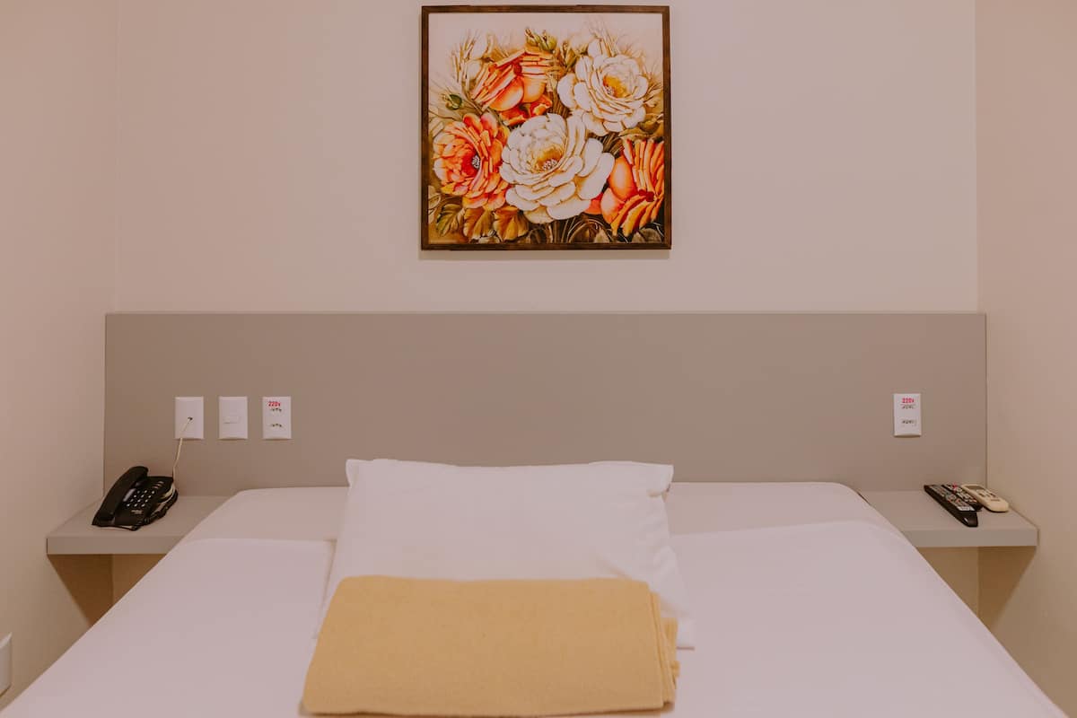 Habitación de hotel con una cama, una mesita de noche con un teléfono y un cuadro colgado en la pared.
