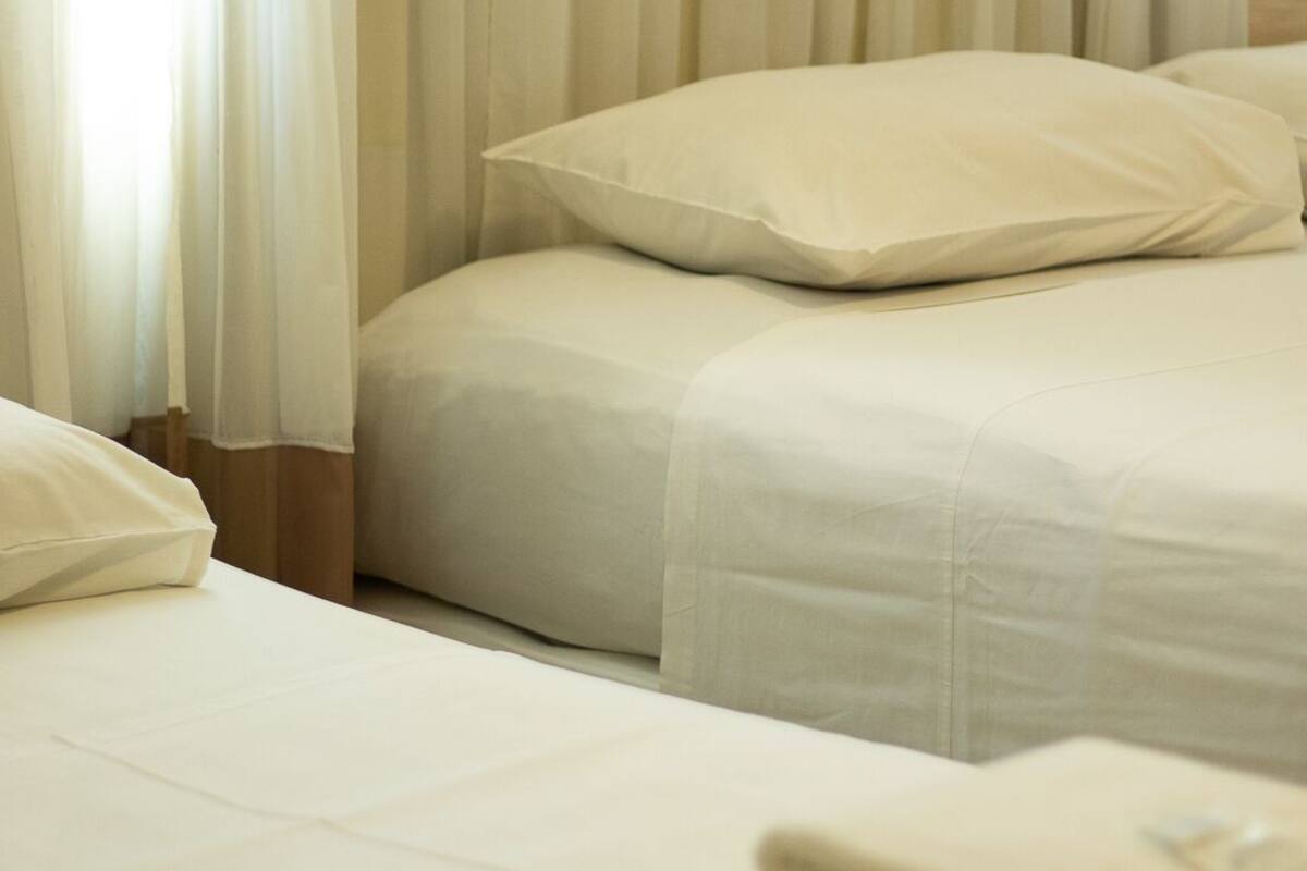 Habitación de hotel con dos camas, ropa de cama blanca y una ventana con cortinas translúcidas.