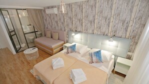 Et hotelværelse med en seng, en sofa, et lille bord og et bruseområde med glasvægge.