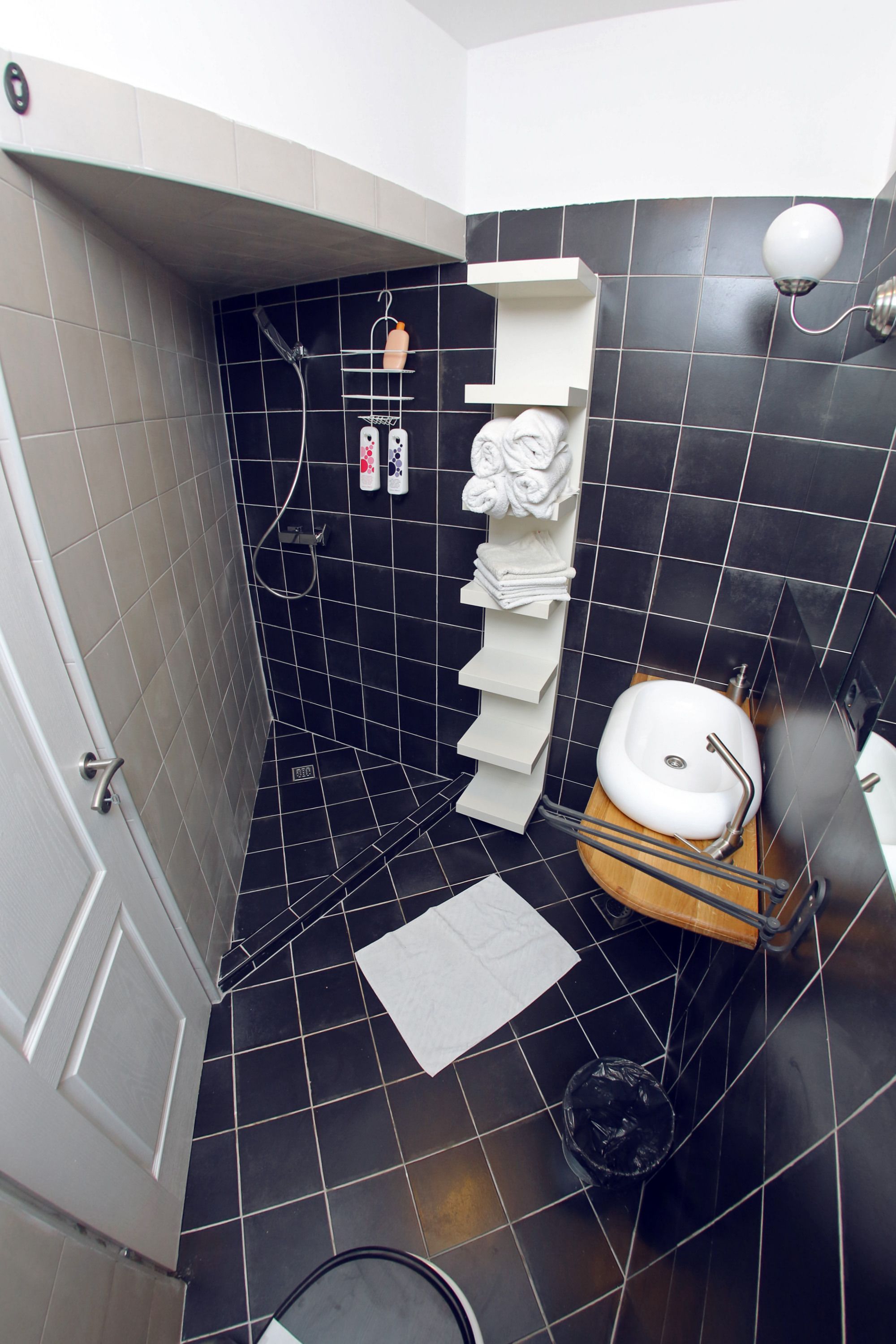 Ein Badezimmer mit schwarzen Fliesen, einem weißen Waschbecken, einer Dusche und einem Handtuchhalter.