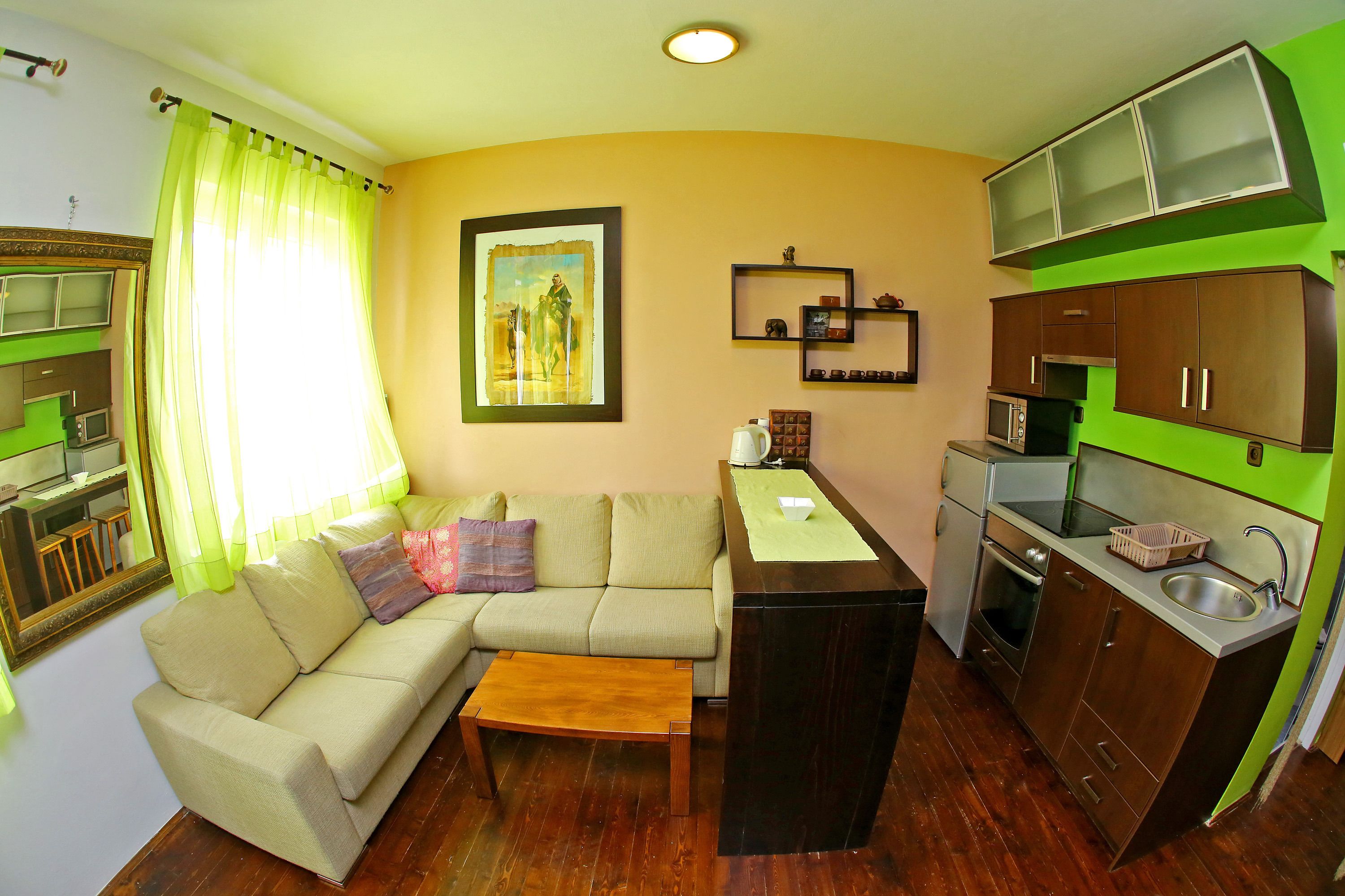 A compact living space with a sofa, coffee table, kitchenette, and a painting on the wall.