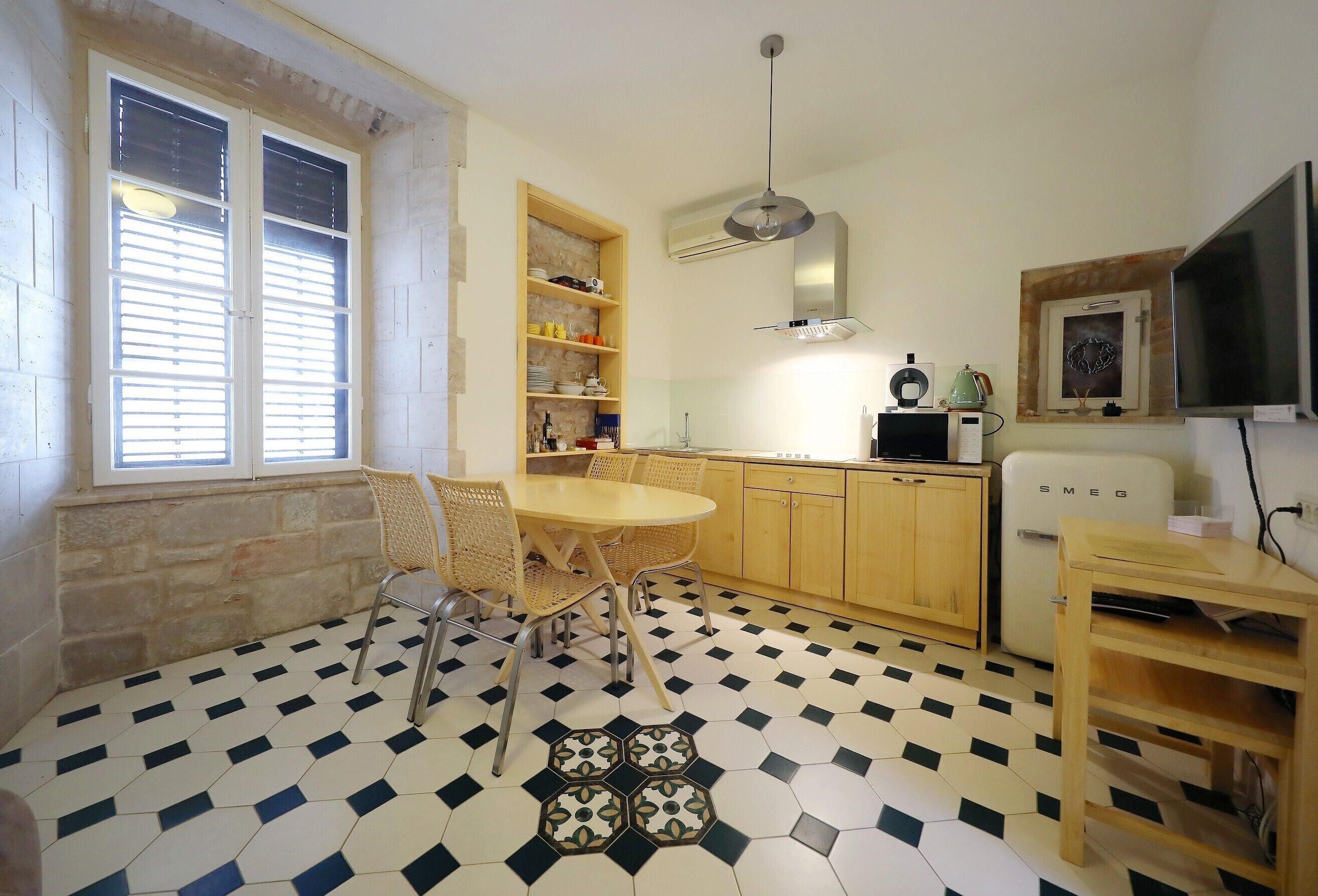 Une cuisine compacte avec un coin repas, dotée d’un sol à carreaux, de meubles en bois et d’une étagère intégrée.