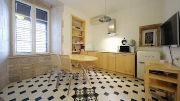 Une cuisine compacte avec un coin repas, dotée d’un sol à carreaux, de meubles en bois et d’une étagère intégrée.
