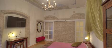 Une chambre à coucher avec un grand lit, un lustre, une télévision, un banc et une porte à panneaux de verre.