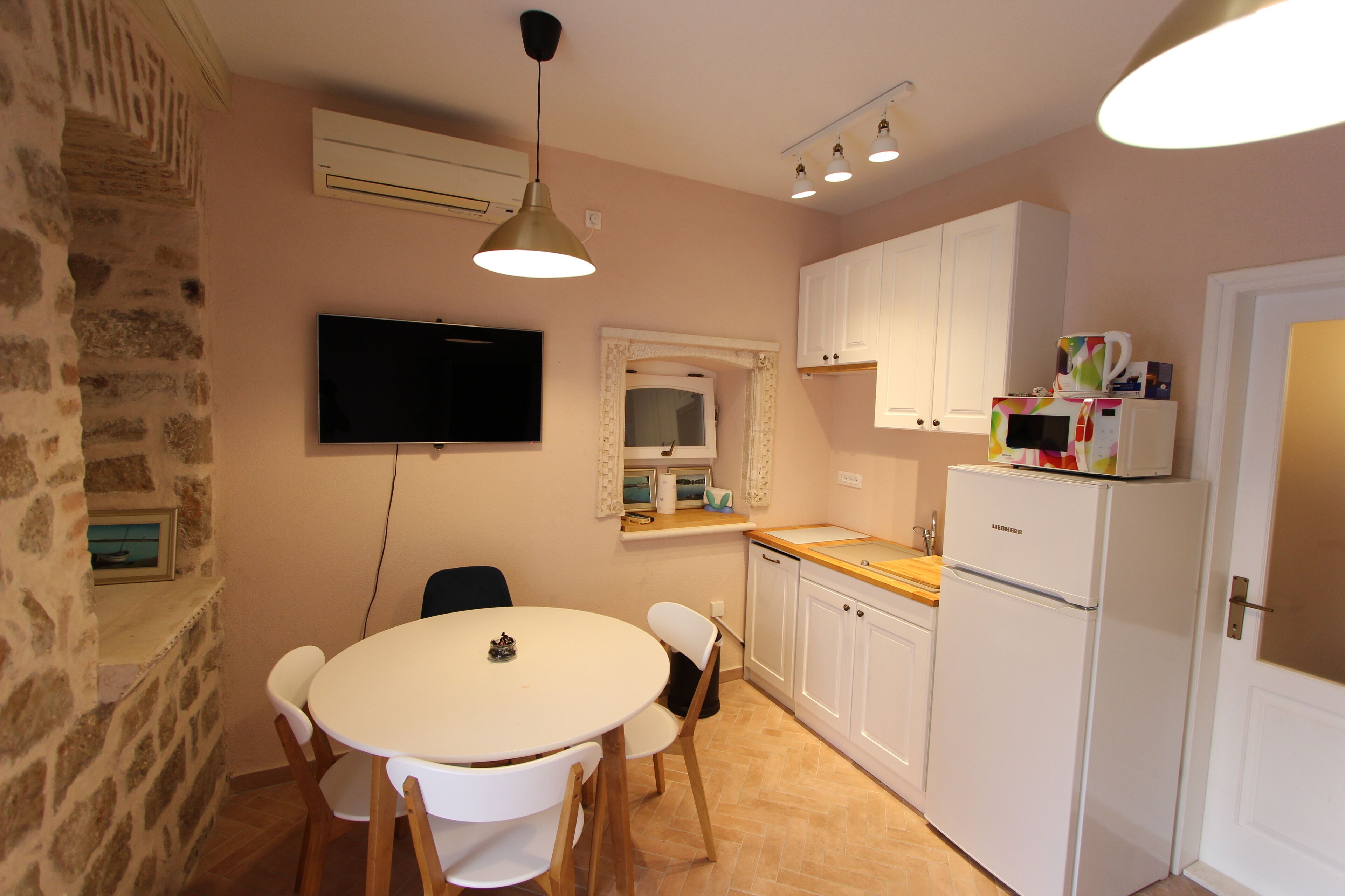 A compact kitchen with white cabinets, a built-in microwave, and a dining area with a round table and chairs.