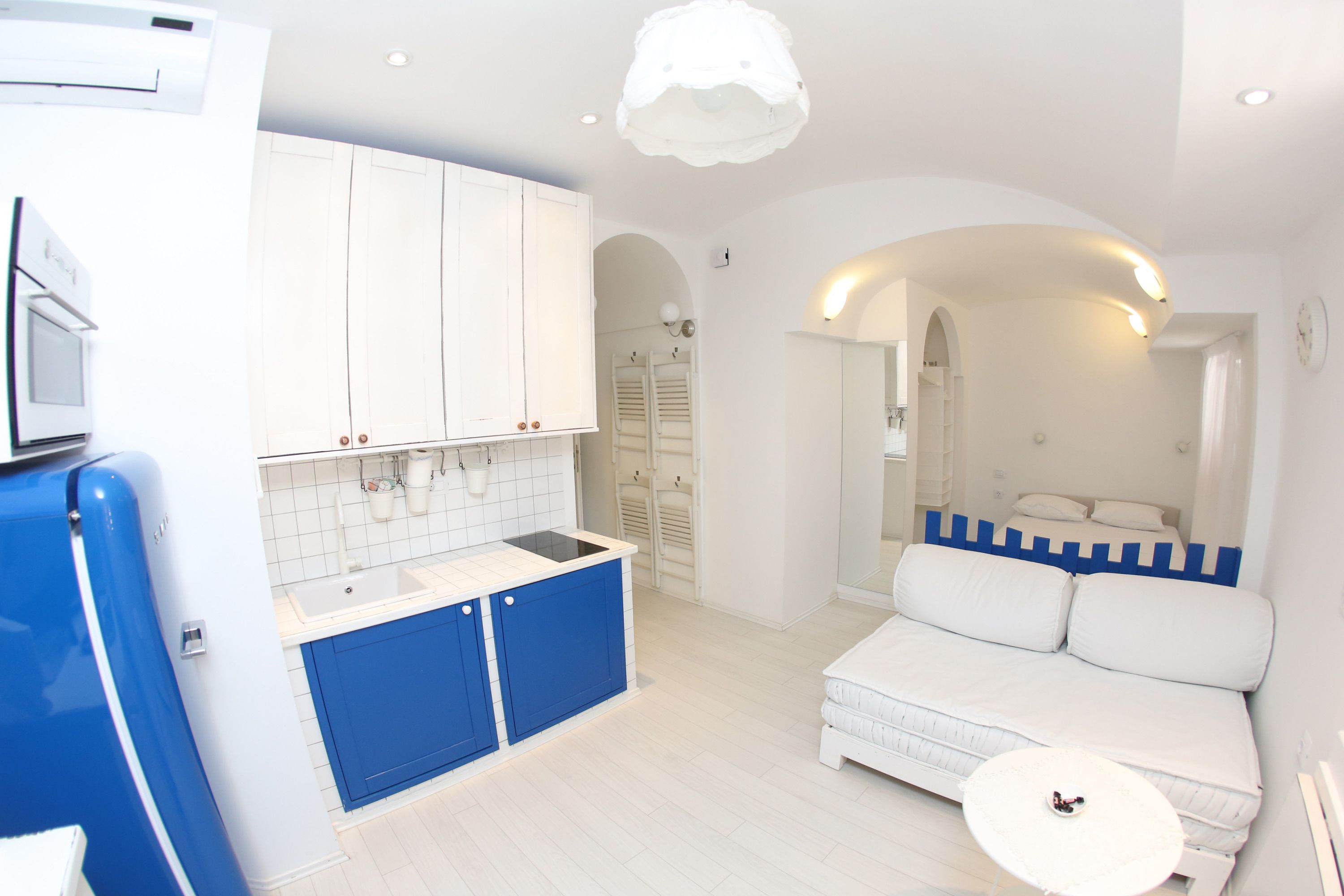 A compact, modern room with a kitchenette, a bed with a blue accent wall, and a small round table.