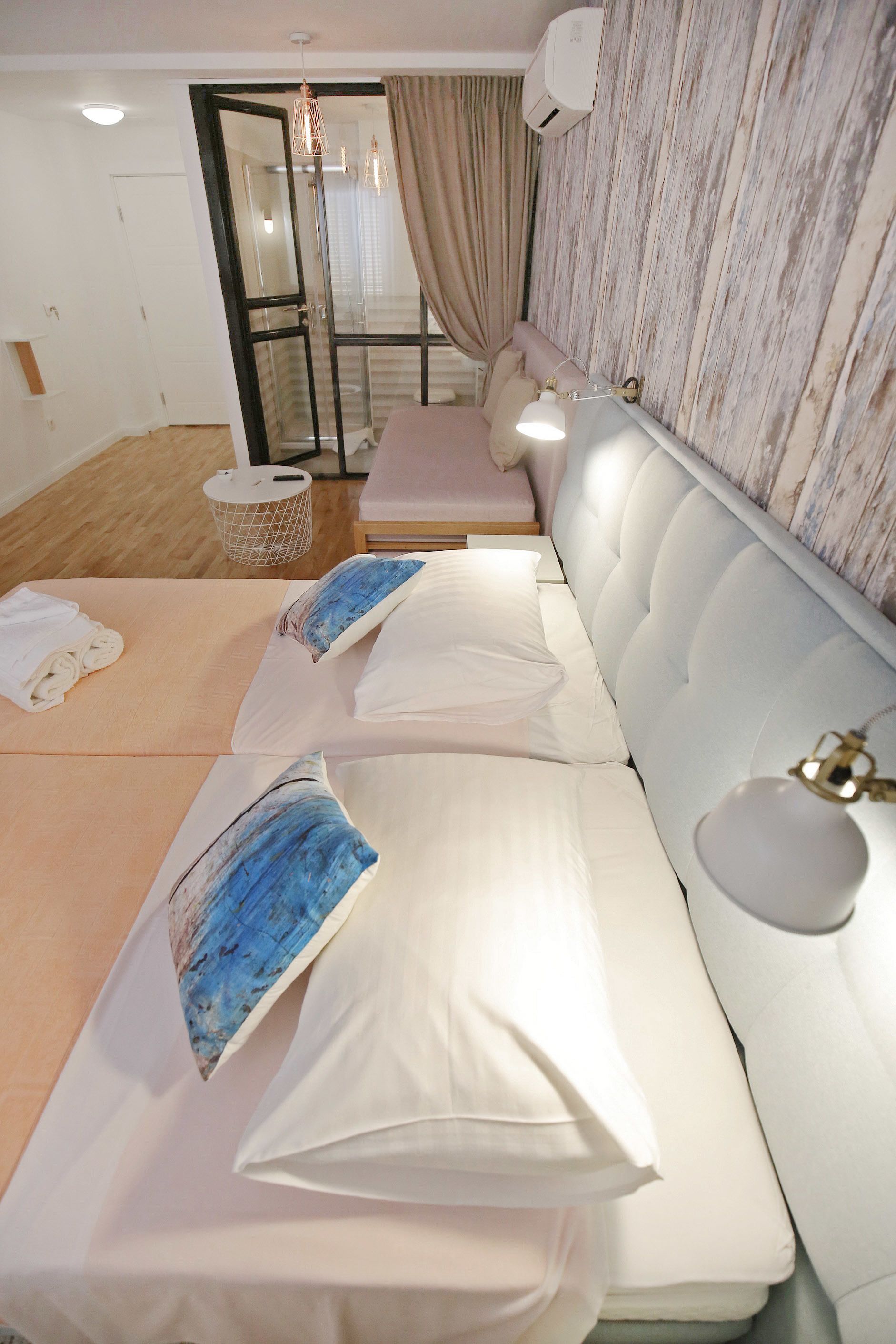 A hotel room with a sofa bed, a small table, a trash bin, and a window with curtains.
