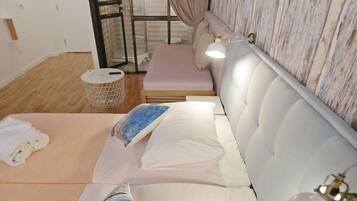 A hotel room with a sofa bed, a small table, a trash bin, and a window with curtains.