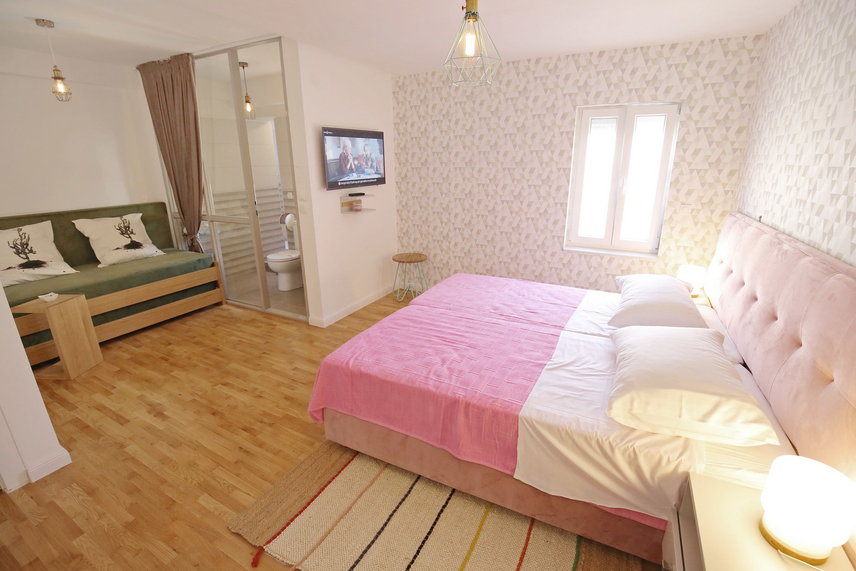 A bedroom with a bed, a sofa, a television, and a window.