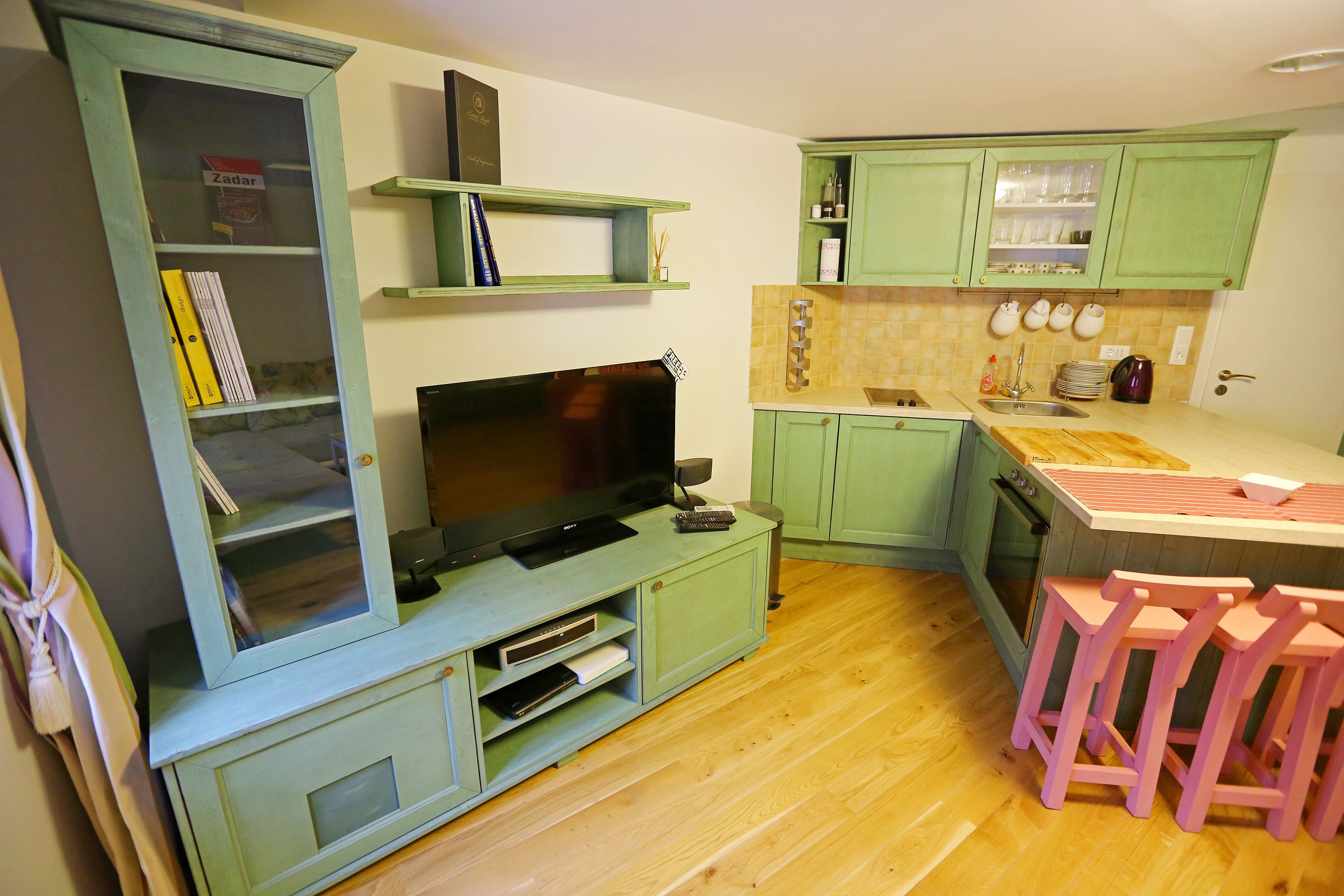 Una cucina compatta con TV, sgabelli da bar in legno e mobili verdi.