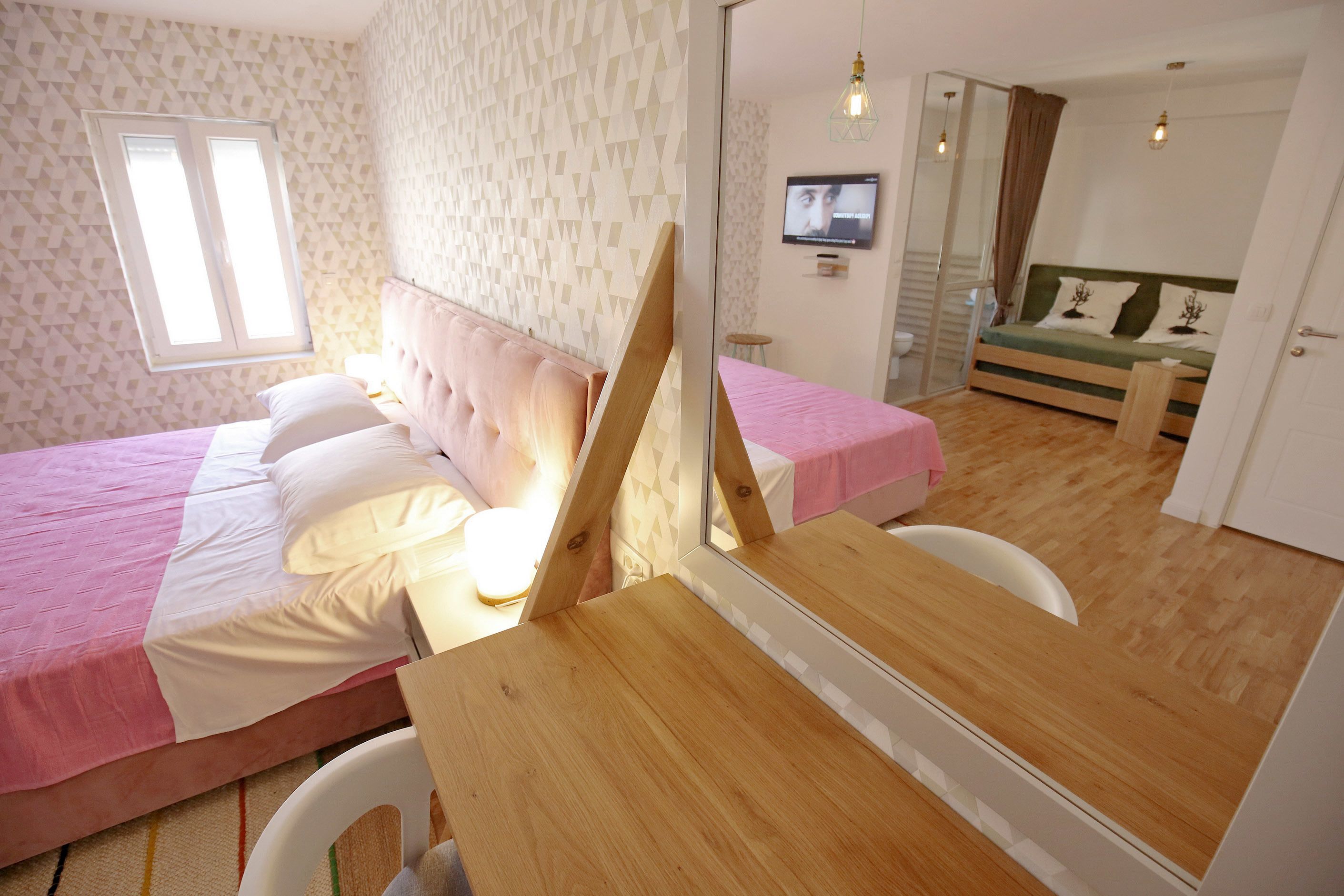 A bedroom with a bed, a mirror, a TV, and a wooden table.