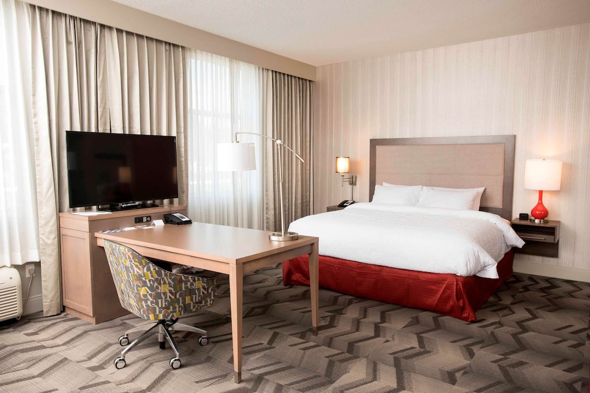 Ein Hotelzimmer mit einem Bett, einem Schreibtisch mit Stuhl, einem Fernseher und einer Lampe.
