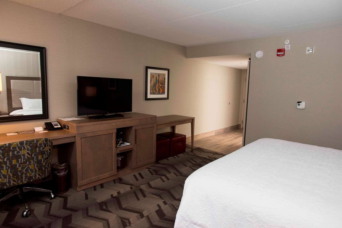 Ein Hotelzimmer mit Bett, Schreibtisch mit Fernseher, Stuhl, Mülleimer und einem gemusterten Teppich.