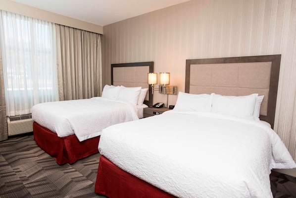 Habitación de hotel con dos camas, cada una con falda roja, ropa de cama blanca y cabecero con lámpara.
