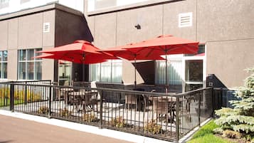 An outdoor patio with red umbrellas, outdoor seating, and a metal fence.