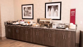 A kitchen counter with various appliances and food items, framed pictures on the wall, and a red sign.