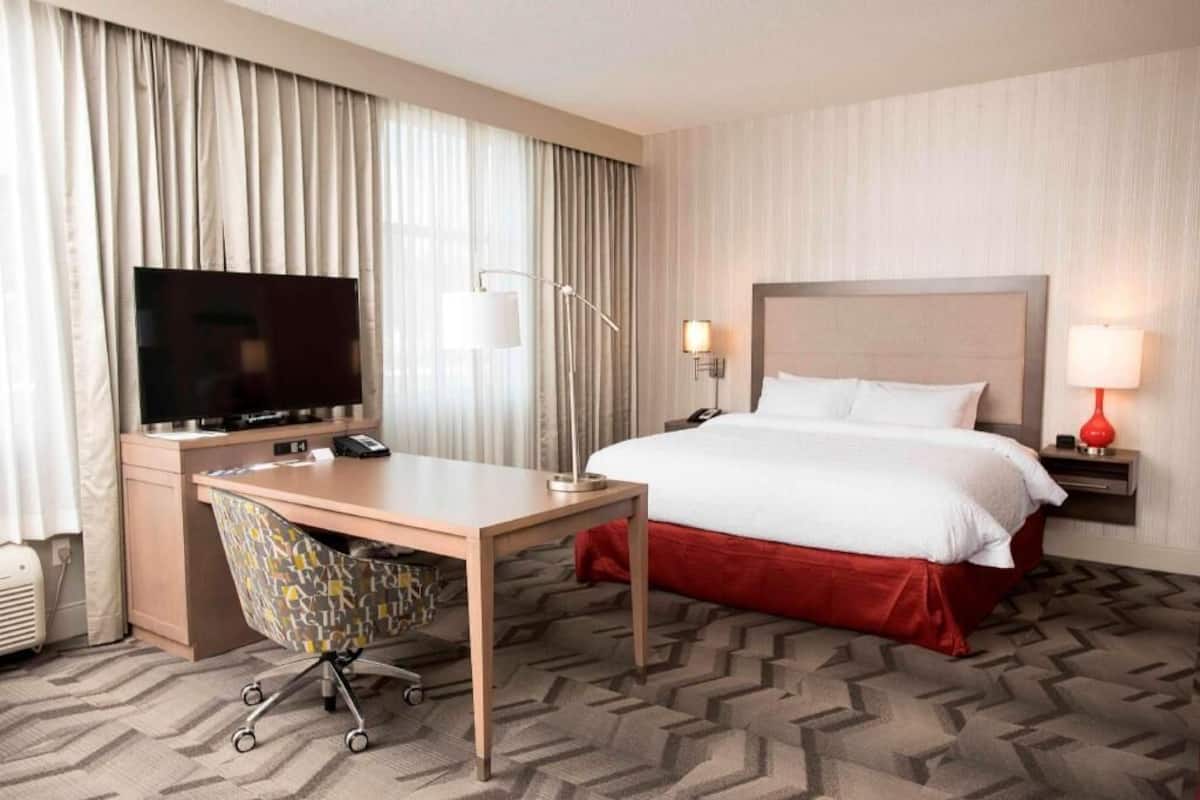 Ein Hotelzimmer mit Bett, Schreibtisch, Stuhl, Fernseher und Lampen.