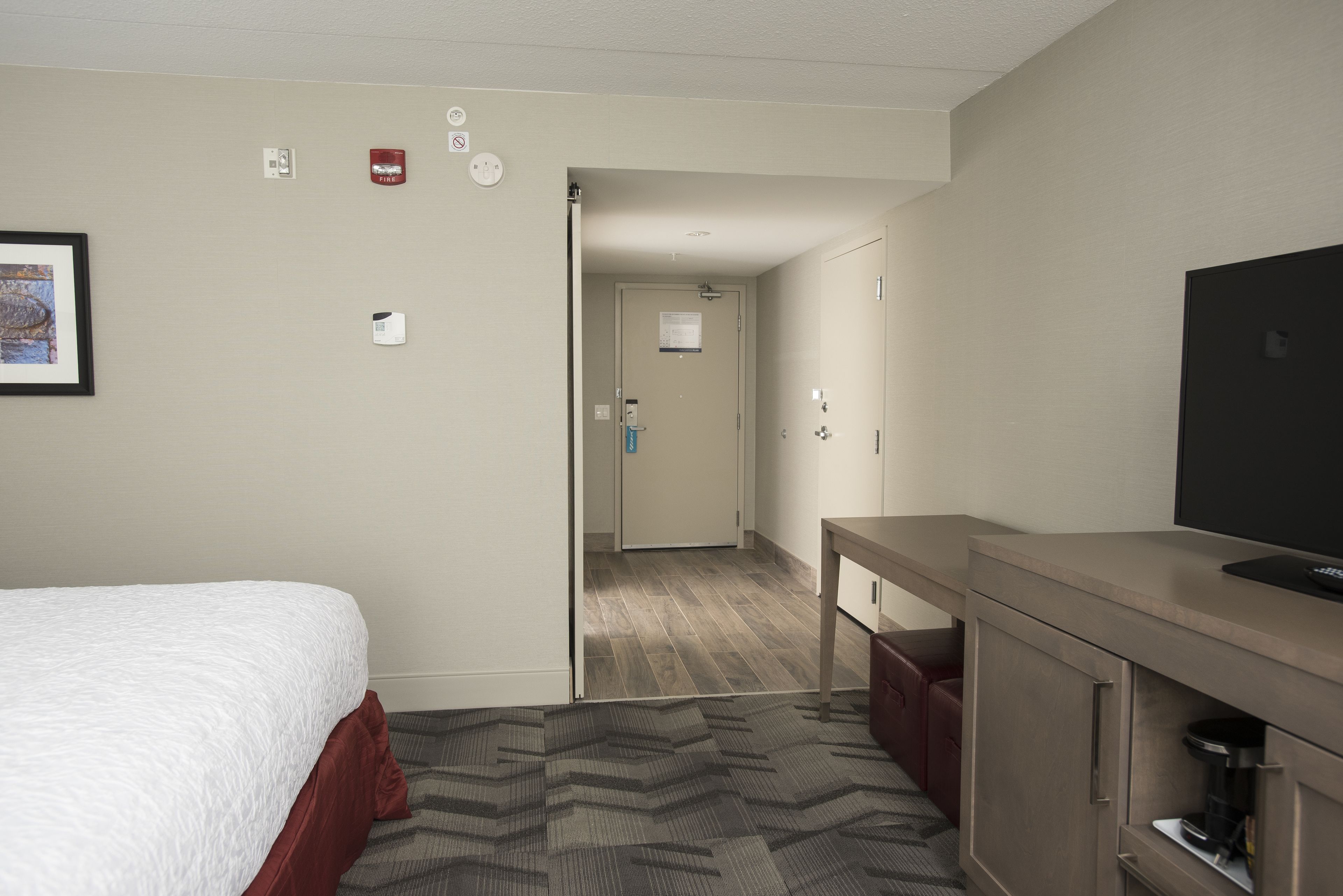 A hotel room with a bed, a desk, a television, and a door leading to another room.