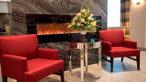 Un vestíbulo moderno con una pared de mármol, una chimenea y dos sillones rojos.