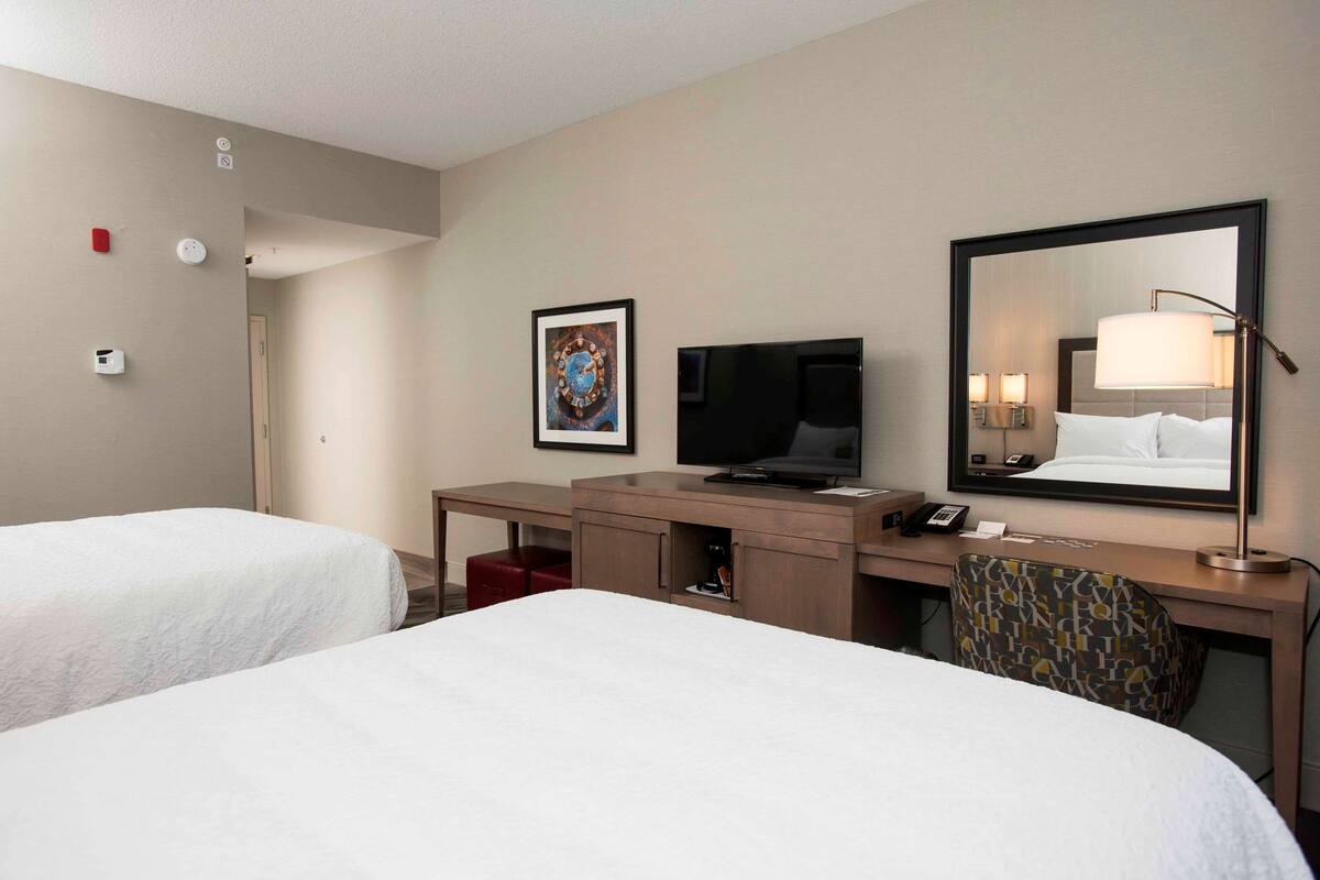 Ein Hotelzimmer mit zwei Betten, einem Schreibtisch mit Fernseher, einem Spiegel und einem roten Sessel.