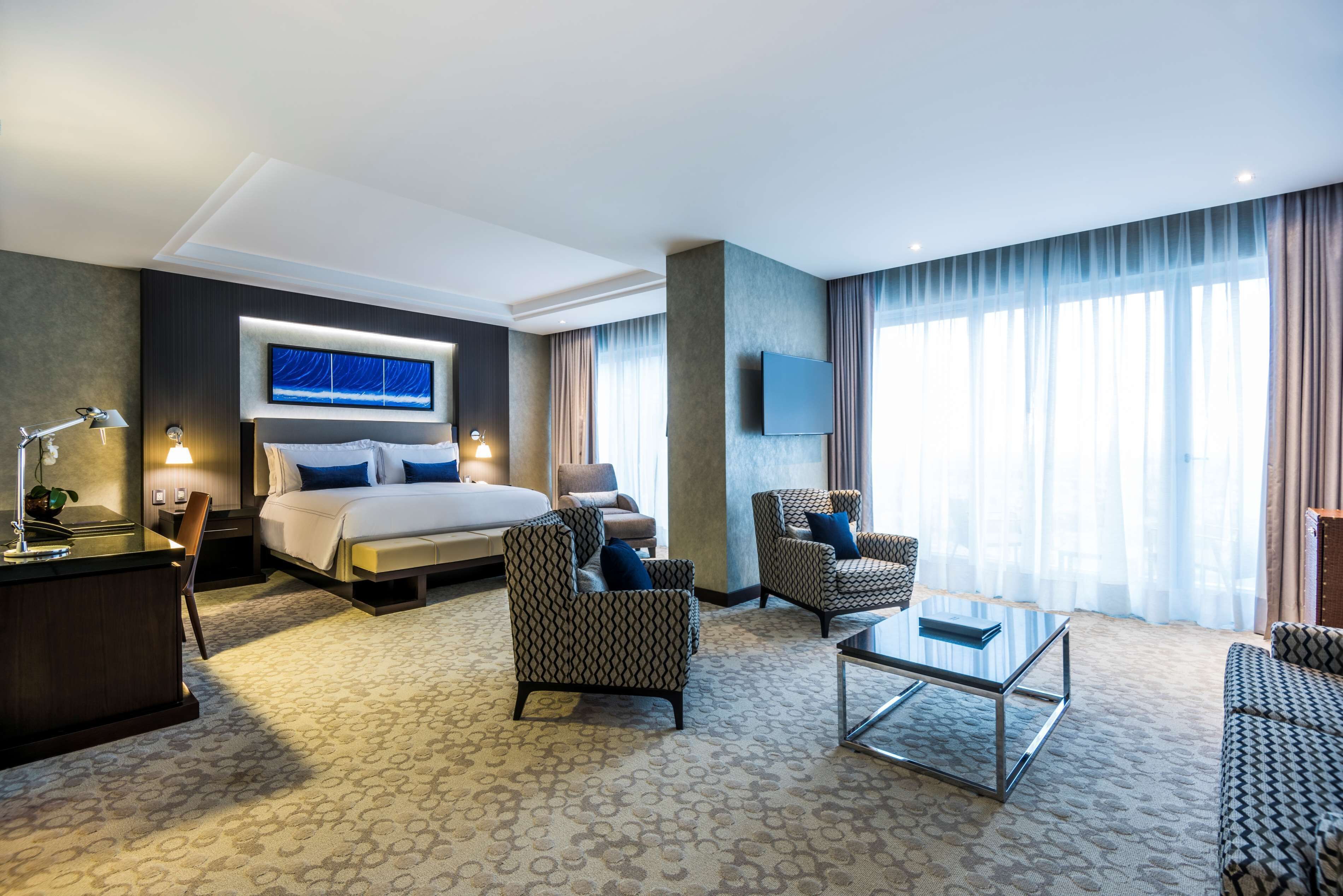 Une chambre d’hôtel avec un grand lit, deux fauteuils, une table basse, une télévision et un bureau avec une lampe.