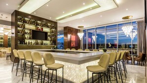 A modern bar area with a large island bar, multiple seating options, and a view of the cityscape through large windows. - Hyatt Regency San Luis Potosi (San Luis Potosi)