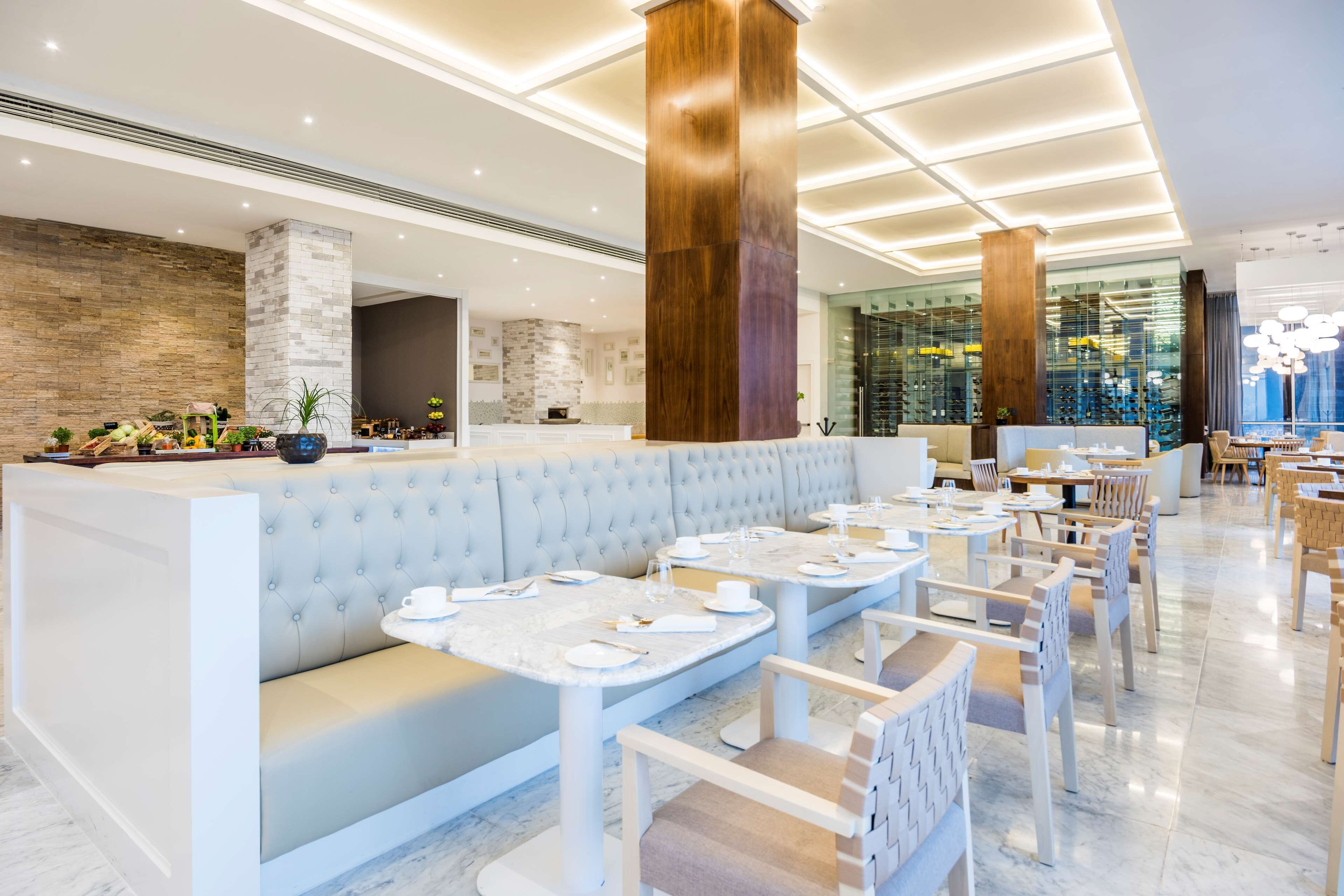 Un restaurante moderno con un largo banco blanco, mesas redondas y una pared de piedra.